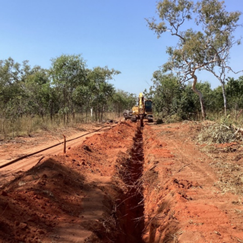 A trench being dug into red earth in preparation for new pipe.