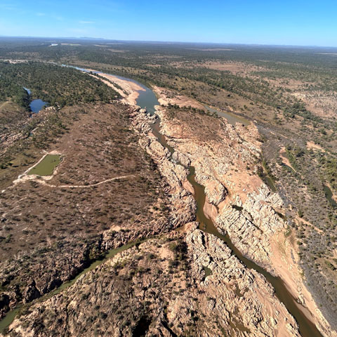 Ariel view of a water channel running surrounded by rocky ground and bushland.