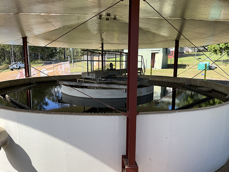 A large water clarification tank in Cherbourg’s Water Treatment Plant, filled with water. The tank structure is under a roof and is white and circular, surrounded by dark red poles.