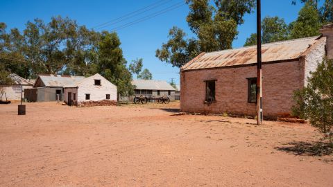 Landscape view of old Hermannsburg historic precinct in NT outback Australia – red dirt in the foreground and old buildings in the background.