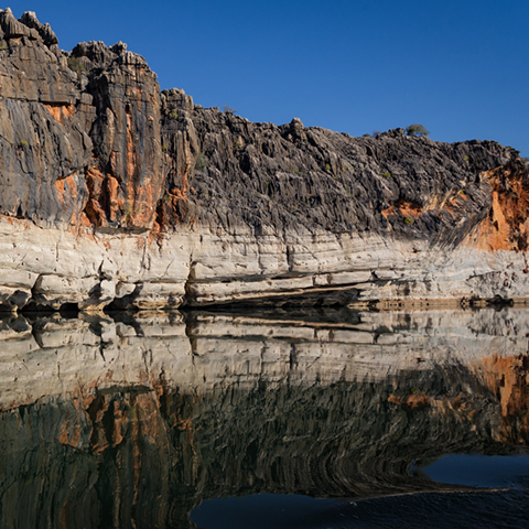 Gorge in Fitzroy Crossing in Western Australia with layered cliff in the background and water in the foreground.