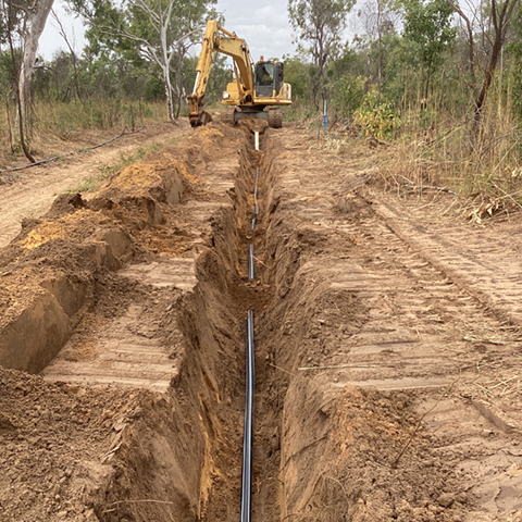 A trench being dug by a crane in bushland.