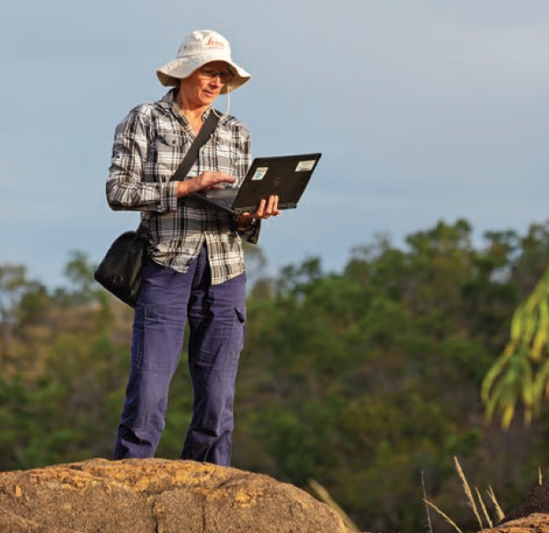 Photograph of a researcher standing, wearing a hat and holding a laptop.