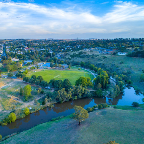 Aerial view of Yass River and township at sunset with green trees and grass on the bank of the river.